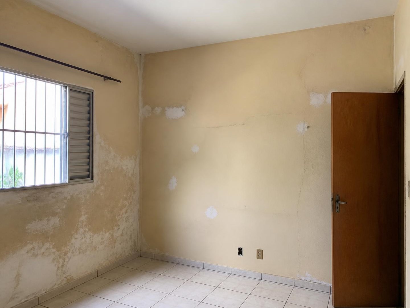 Quarto com paredes manchadas, trincas e remendos de massa antes da pintura