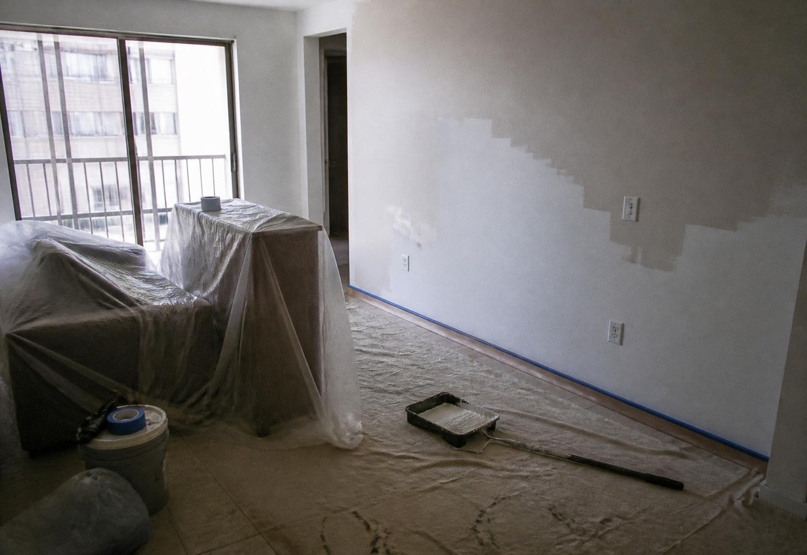Sala de apartamento com móveis cobertos por lona durante a pintura interna