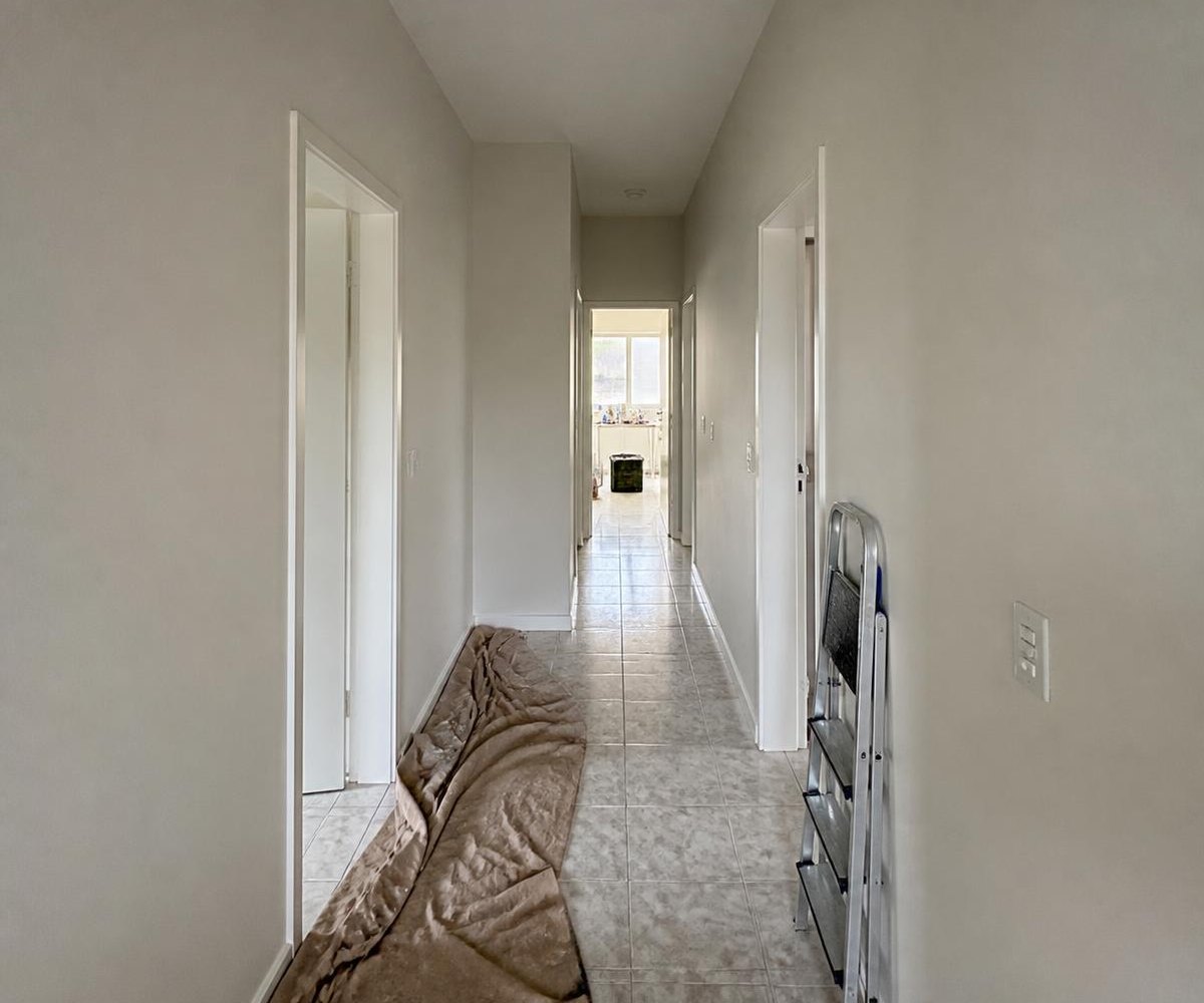 Corredor de casa recém-pintado em off-white, com escada e lona de proteção no piso