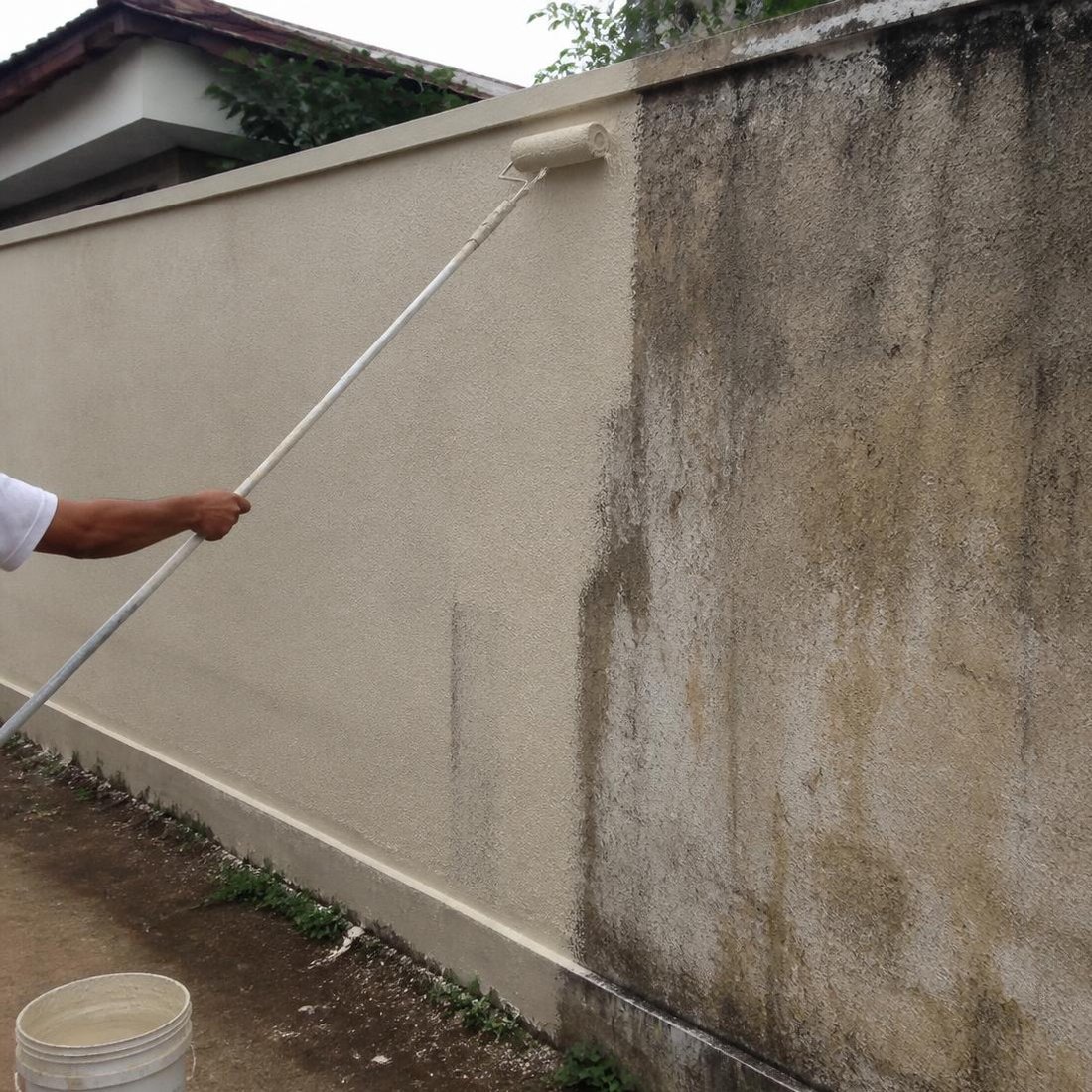 Parede externa e muro em processo de pintura com rolo em extensor